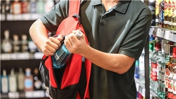 Ein Mann steckt eine Flasche in seinen Rucksack: Diebstahl 