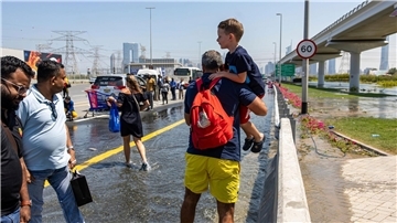 Ein Mann trägt ein Kind durch das von starkem Regen verursachte Hochwasser in Dubai.