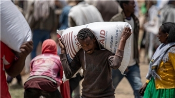 Ein Mann trägt einen Sack Weizen auf den Schultern, der von der Relief Society of Tigray verteilt werden soll.