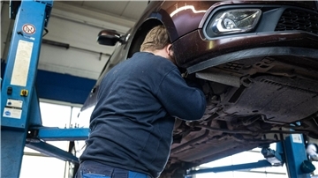 Ein Mechaniker schaut in einer Kfz-Werkstatt in den Radkasten eines Autos.