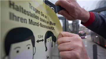 Ein Mitarbeiter der Koblenzer Verkehrsbetriebe entfernt an einer Haltestelle einen Aufkleber, der die Fahrgäste zum Tragen von Masken auffordert.