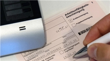 Ein Mitarbeiter einer Arztpraxis notiert etwas auf einer Arbeitsunfähigkeitsbescheinigung.