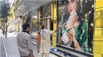 Ein Mitarbeiter eines Schönheitssalons übermalt ein großes Foto einer Frau an der Wand, nachdem die Taliban in die afghanische Hauptstadt eingedrungen sind.