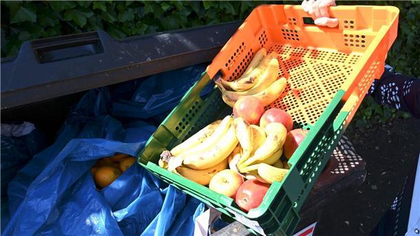 Ein Mitarbeiter eines Supermarktes bringt Obst zu einem Müllcontainer.