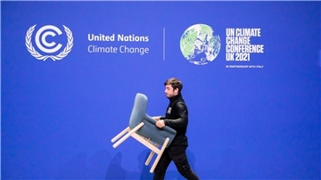 Ein Mitarbeiter trägt bei der UN-Klimakonferenz COP26 einen Stuhl von einer Bühne.