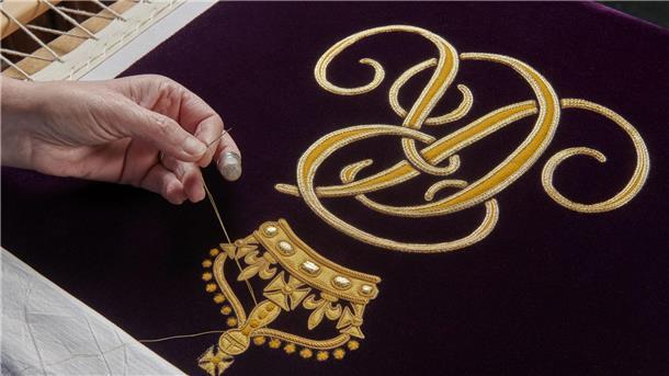 Ein Mitglied der Royal School of Needlework stickt den Schriftzug von Queen Camilla von Hand auf deren Robe.