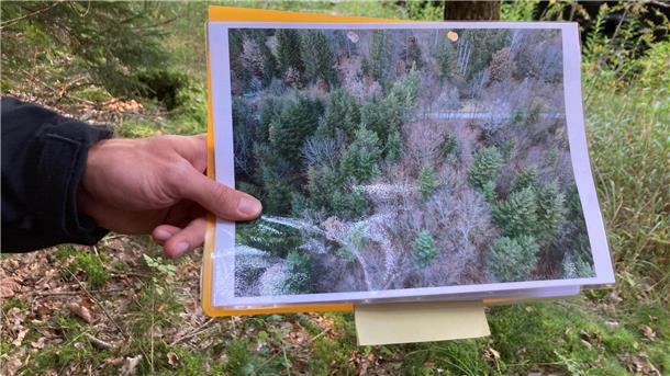 Vermisste Frau: Polizei durchsucht Wald bei München Ein Polizeibeamter hält ein Drohnen-Bild in der Hand.