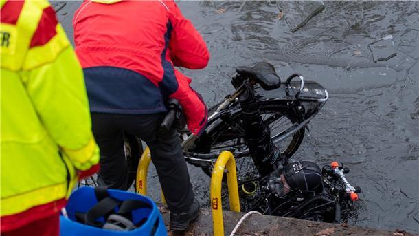 Ein Polizeitaucher hebt ein Fahrrad aus dem Schifffahrtskanal.