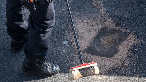 Ein Polizist fegt Sand über die Kleberückstände auf der A100.