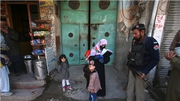 Ein Polizist in Pakistan steht Wache, während einem Kind ein Polio-Impfstoff verabreicht wird.