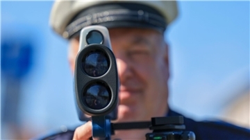 Ein Polizist misst mit einem Laserhandmessgerät (Laserpistole) während einer Geschwindigkeitskontrolle einen Autofahrer.