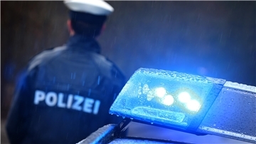 Ein Polizist steht vor einem Streifenwagen dessen Blaulicht aktiviert ist. (Symbolbild)