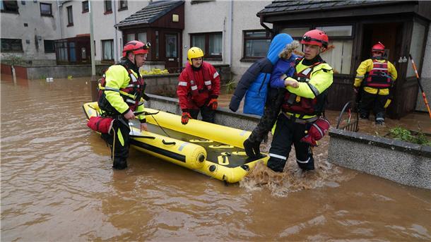 Unwetter an den Küsten (Update #27): Person auf Fehmarn von Baum erschlagen Ein Rettungsmitarbeiter trägt einen Jungen in Brechin (Schottland) aus einem Haus.