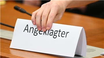 Ein Schild mit der Aufschrift „Angeklagter“ wird auf die Gerichtsbank gestellt.
