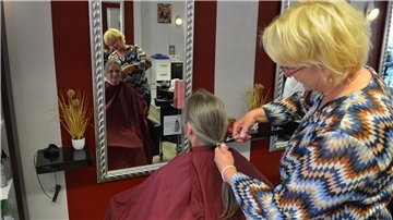 Eine Frau schneidet einer anderen Frau einen Zopf Haare ab.