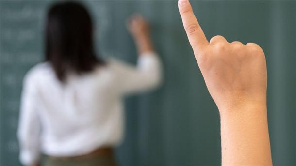 Erster Schultag nach den Sommerferien Ein Schüler meldet sich, während die Lehrerin an die Tafel schreibt.