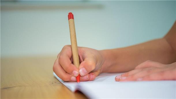 Ministerin: Startchancen-Programm für Bildungsgerechtigkeit Ein Schüler schreibt mit einem Kugelschreiber in sein Heft.