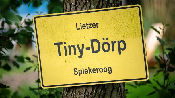 Neben der Schule in Mini-Häusern wohnen Ein selbstgebasteltes Ortsschild hängt am Gelände mit den Mini-Häusern.