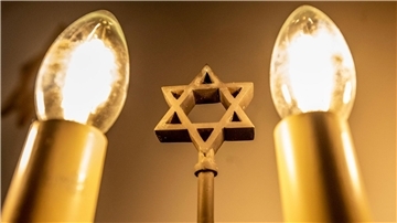 Ein siebenarmiger Leuchter (Menora) mit einem Davidstern in der Mitte leuchtet in einer Synagoge. Fragen zum Judentum werden auf einer Website beantwortet.