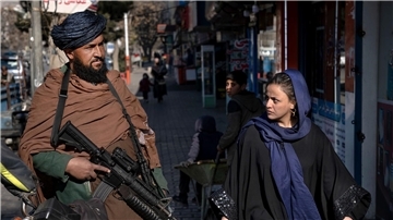 Ein Taliban-Kämpfer steht in Kabul Wache, während eine Frau vorbeiläuft. (Archivbild)