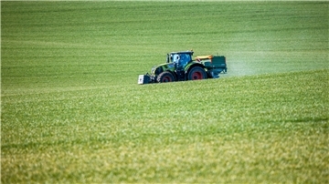 Ein Traktor mit einem Streuaufsatz verteilt Dünger auf einem Feld. Viele Landwirte haben mit massiv gestiegenen Kosten für Düngemittel zu kämpfen.