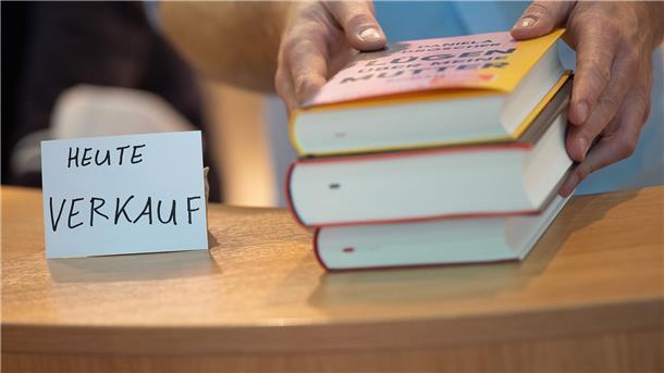 Ein Verkäufer gibt während der Frankfurter Buchmesse am Stand von Kiepenheuer & Witsch Bücher über den Tisch.