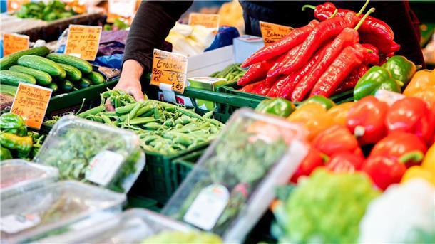 Ifo: Einige Firmen nutzen Inflation für Gewinnsteigerung Ein Verkäufer greift an einem Obst- und Gemüsestand auf dem Wochenmarkt in eine Kiste mit Erbsen.