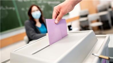 Ein Wähler wirft in einem Wahllokal, das im Klassenraum einer Schule untergebracht ist, seinen Stimmzettel für die Kommunalwahl in die Wahlurne.