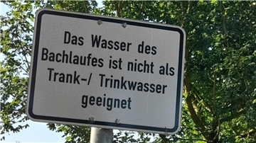 Ein Schild auf dem steht: "Das Wasser des Bachlaufes ist nicht als Trank-/Trinkwasser geeignet"