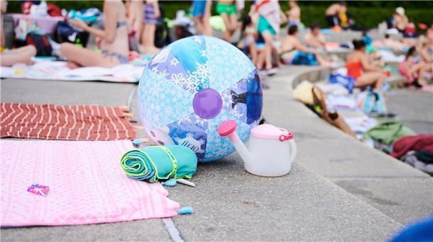 Ein Wasserball und Handtücher liegen in einem Schwimmbad am Beckenrand.