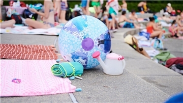 Ein Wasserball und Handtücher liegen in einem Schwimmbad am Beckenrand.