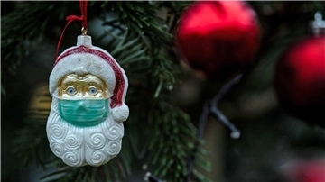 Ein Weihnachtsmann mit einer Schutzmaske hängt als Weihnachtsbaumschmuck in einem Tannenbaum.