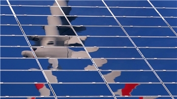 Ein Windrad spiegelt sich in einer Solar-Anlage.