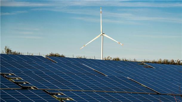 Erneuerbare Energien decken Hälfte des Stromverbrauchs Ein Windrad steht auf einem Hügel einer großflächigen Solaranlage.