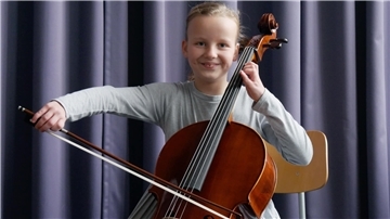 Ein Mädchen spielt auf einem Streichinstrument und strahlt.