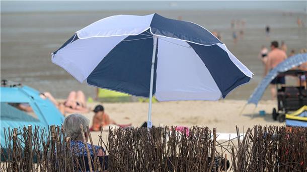 Eine ältere Frau sitzt sommerlichem am Badestrand unter ihrem Sonnenschirm.