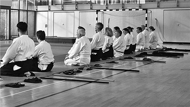 Eine Gruppe Kampfsportler sitzt auf Knien in der Sporthalle