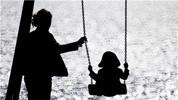 Eine alleinerziehende Mutter schaukelt ihr Kind auf einem Spielplatz.