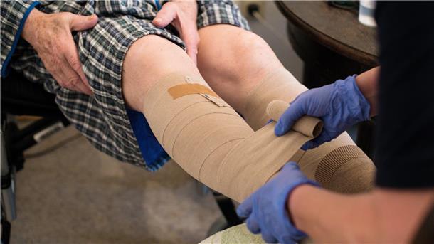 Eine ambulante Pflegerin bandagiert die Beine eines alten Mannes. Im Landkreis Rotenburg ist es zunehmend schwierig, Menschen für solche Tätigkeiten zu finden. Das geht aus dem ersten Pflegebericht hervor, mit dem sich derzeit der Kreistag befasst.