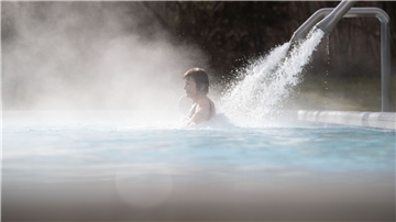 Eine Besucherin steht unter einem Wasserstrahl.
