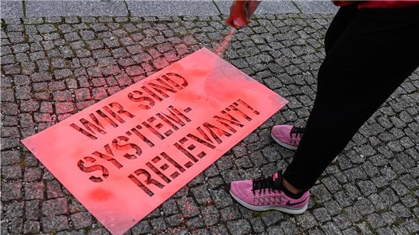 Eine Demonstrantin sprüht vor dem Verhandlungsort der Tarifrunde im öffentlichen Dienst von Bund und Kommunen 2020 mit einer Schablone die Worte "Wir sind system-relevant" auf den Boden.