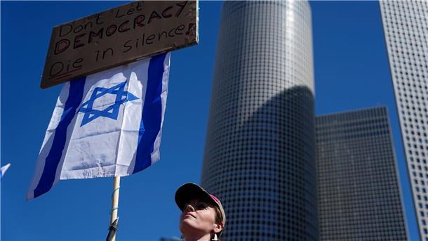 Eine Demonstrierende hält eine israelische Flagge und ein Plakat mit der Aufschrift „Lasst die Demokratie nicht schweigend sterben!“.