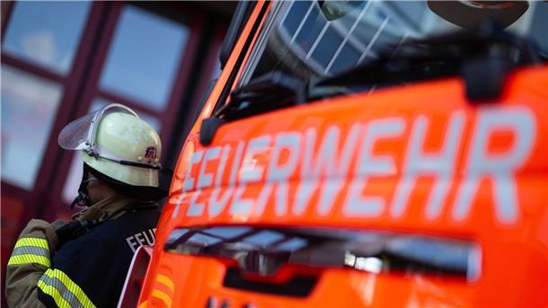 Eine Einsatzkraft der Feuerwehr steht neben einem Einsatzfahrzeug der Feuerwehr.