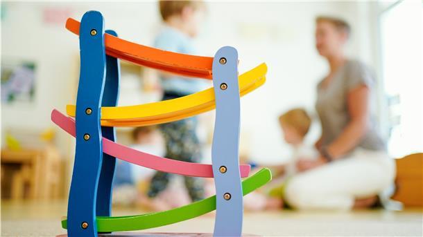 Eine Erzieherin spielt in einer Kindertagesstätte hinter einer Rollbahn mit Kindern. Erzieher werden dringend gesucht, in der gesamten Region.