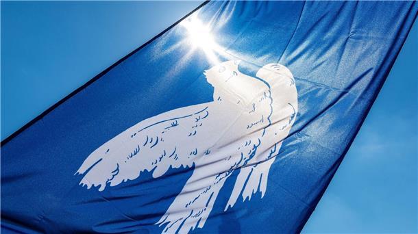 Eine Fahne mit einer Friedenstaube verdeckt die Sonne.