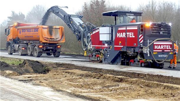 Eine Fräse entfernt Asphalt und Beton von der Fahrbahn. Das Baterial wird in einen vorausfahrenden Lkw geschleudert. 