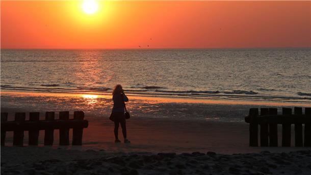 Von Feuershow bis Wattwanderung: Inseln feiern Mittsommer Eine Frau fotografiert am Strand der Insel Wangerooge einen Sonnenuntergang.