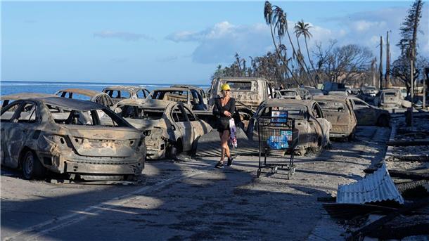 Nach tödlichen Bränden auf Maui: Klage gegen Stromversorger Eine Frau geht an zurückgebliebenen Trümmern nach dem Waldbrand in Lahaina vorbei.