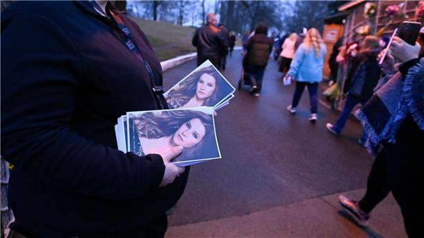 Eine Frau hält Flyer mit einem Bild von Lisa Marie Presley, während Menschen an ihr vorbeigehen, um in Graceland an einem Gedenkgottesdienst teilzunehmen.