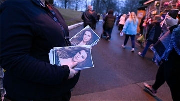 Eine Frau hält Flyer mit einem Bild von Lisa Marie Presley, während Menschen an ihr vorbeigehen, um in Graceland an einem Gedenkgottesdienst teilzunehmen.